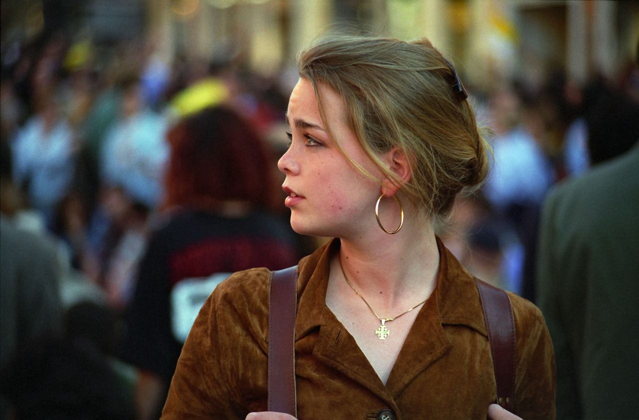 a woman standing in front of a crowd of people, by Eva Gonzalès, flickr, chloe moretz, 2 0 0 1, round jawline, pensive