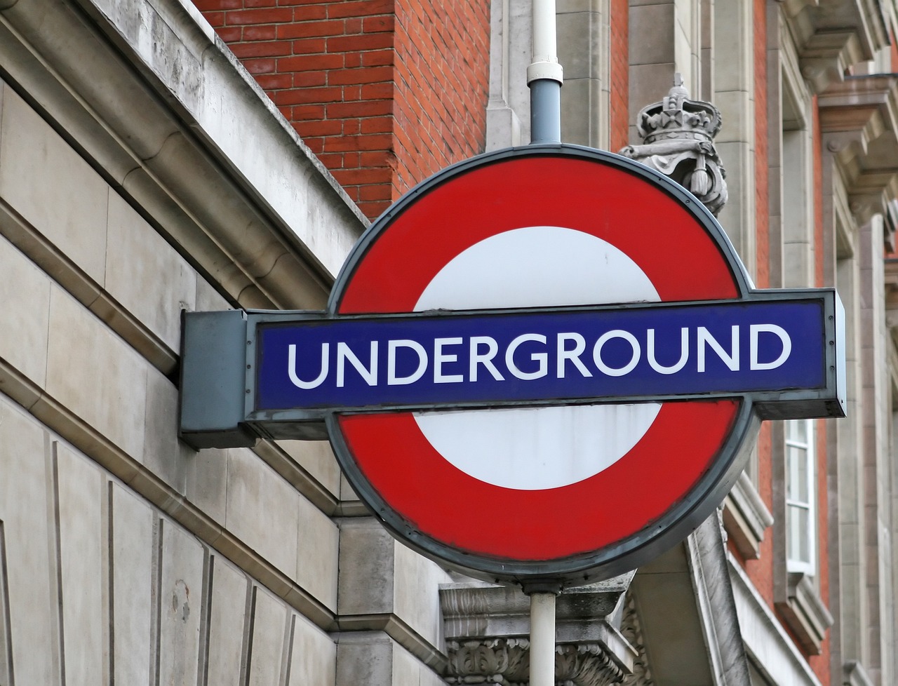 a blue and white sign hanging from the side of a building, a picture, by Peter Prendergast, shutterstock, underground comix, round logo, train in a tunnel, reddish, silver