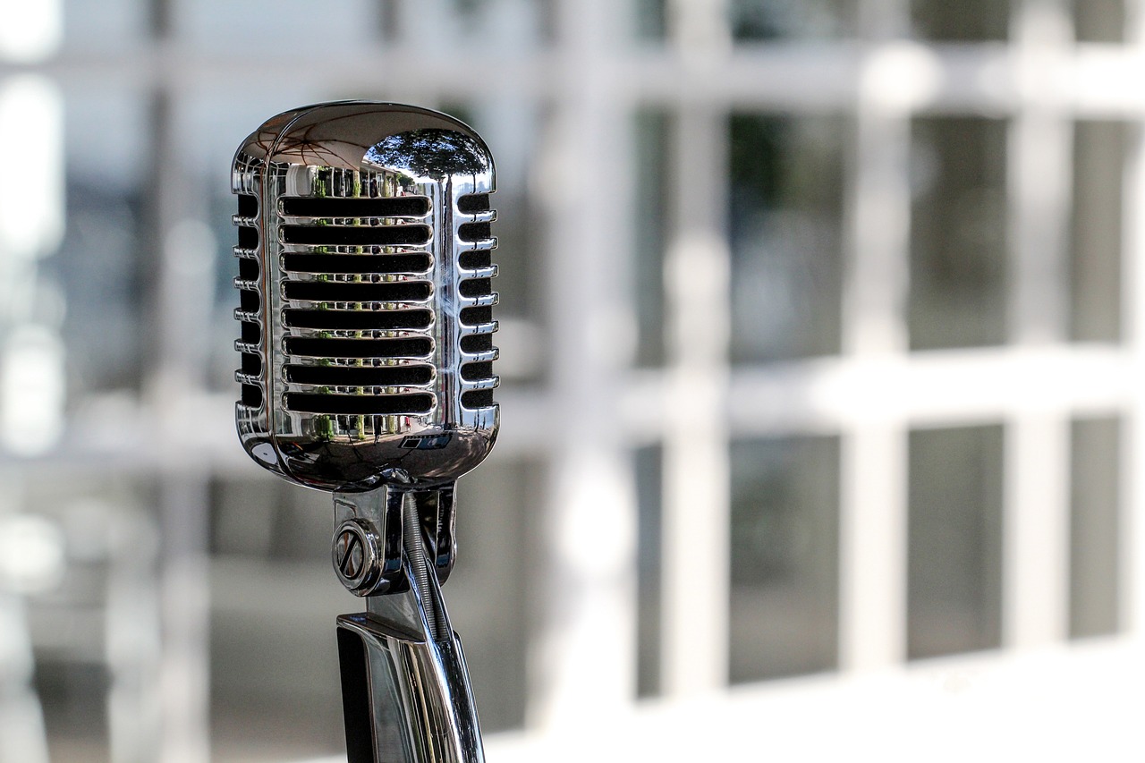 a close up of a microphone with a building in the background, a portrait, pixabay, purism, sparkling in the sunlight, museum quality photo, table with microphones, wikimedia commons