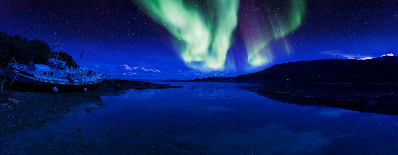 a boat sitting on top of a beach next to a body of water, by Ejnar Nielsen, shutterstock, northern lights in space, blue reflections, light show, paul barson