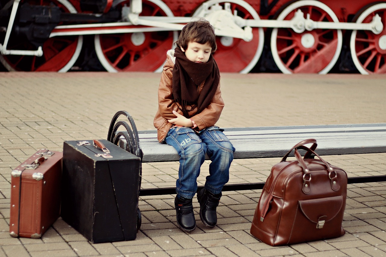 a little boy sitting on a bench next to two suitcases, happening, brown boots, train station, sofya emelenko, wearing leather