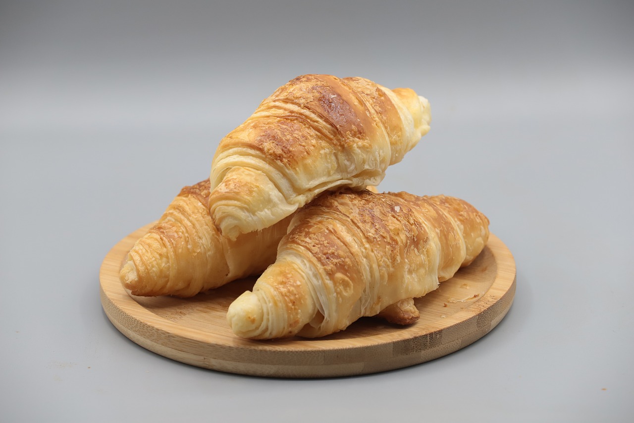 a couple of croissants sitting on top of a wooden plate, photorealism, on a gray background, high quality product photo, hot food, the photo shows a large