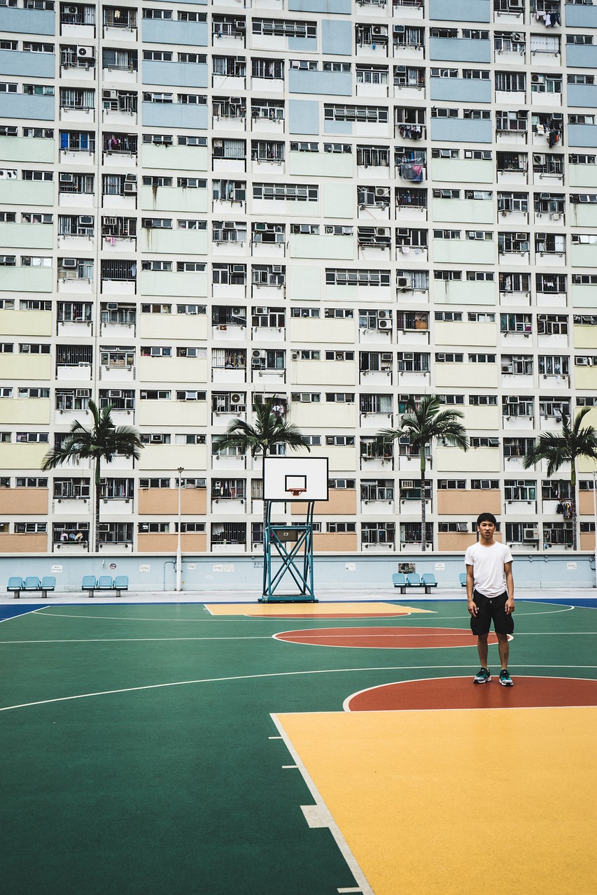 a man standing on top of a basketball court next to a tall building, by Patrick Ching, postminimalism, looking at the camera, volley court background, standing in township street, on a football field