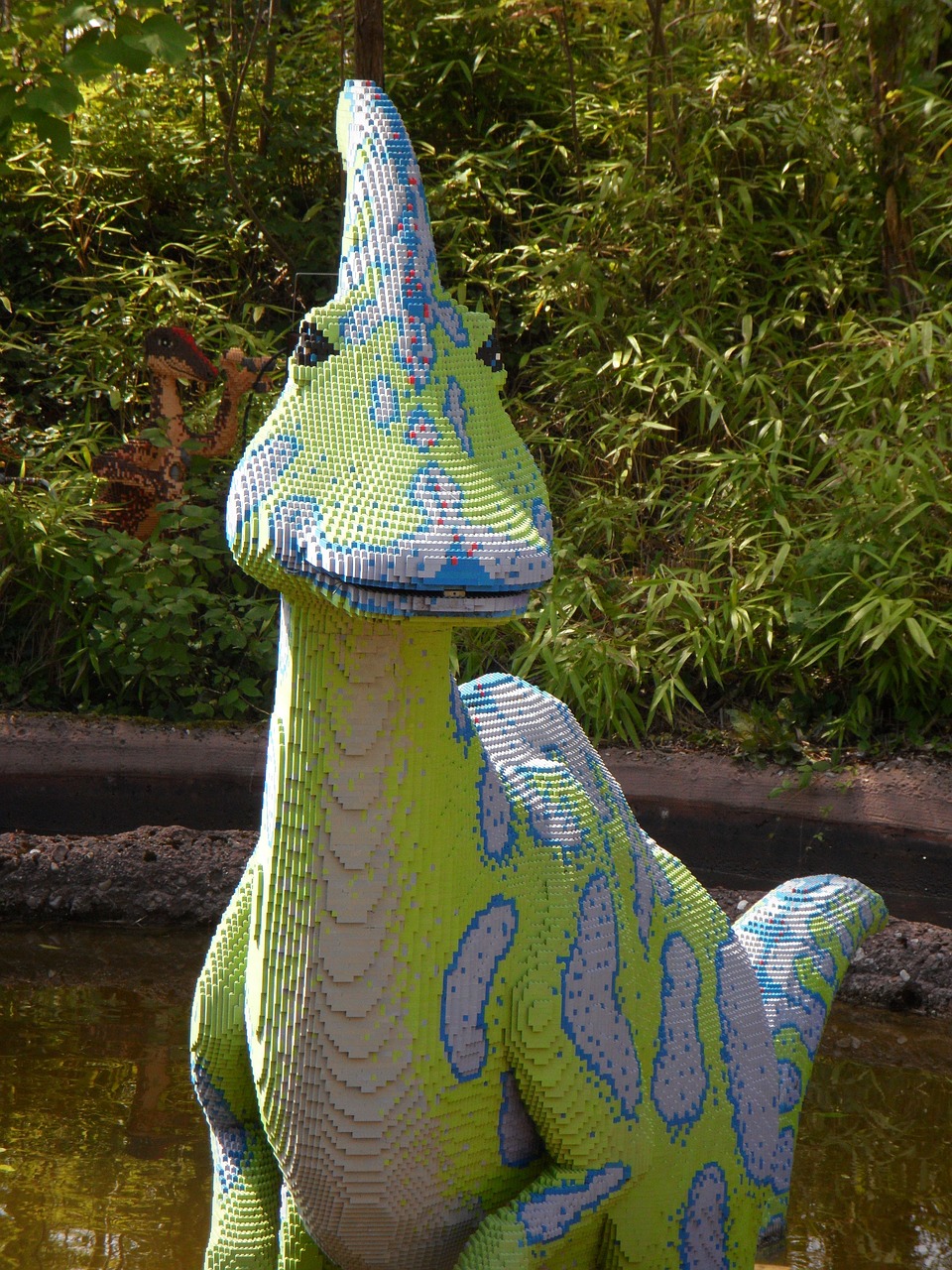 a statue of a dinosaur sitting next to a body of water, inspired by Abidin Dino, flickr, made out of legos, swirl, but very good looking”, he has an elongated head shape