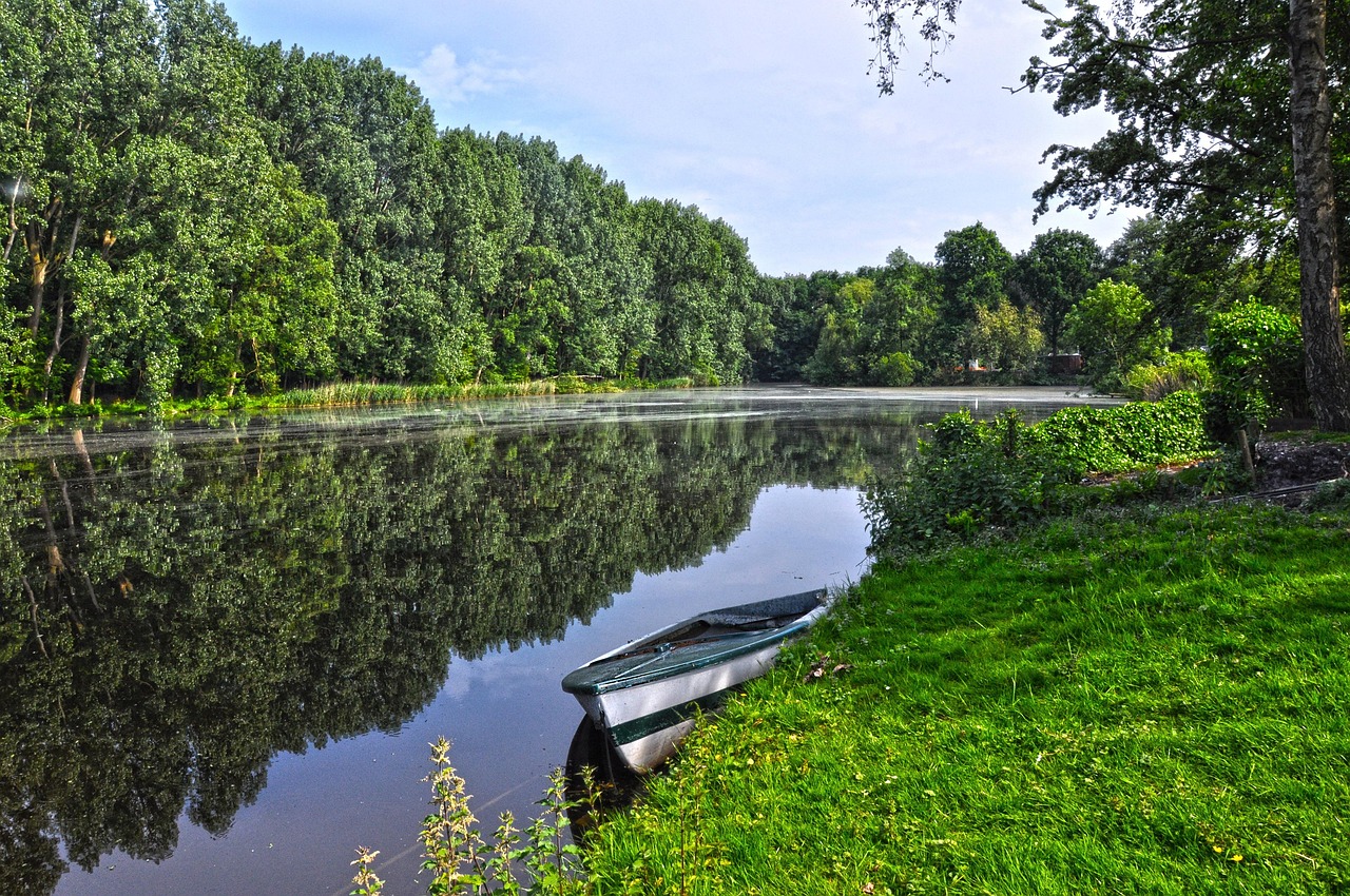 a boat sitting on top of a lush green field, a picture, inspired by Meindert Hobbema, pixabay, in a park and next to a lake, reflections on the river, helmond, beautiful morning