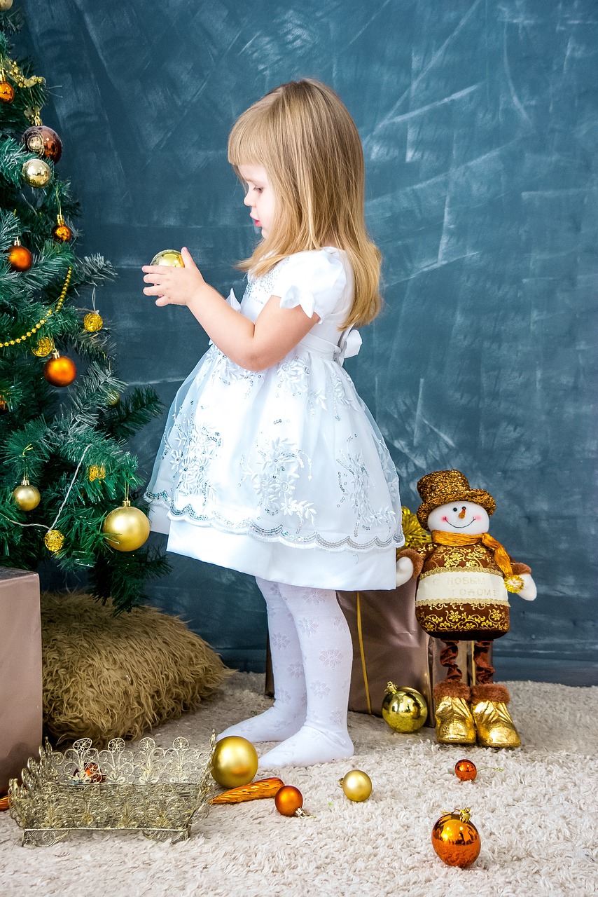 a little girl standing in front of a christmas tree, a picture, by Maksimilijan Vanka, shutterstock, process art, pretty white dress, white tights, golden and silver colors, toy photo