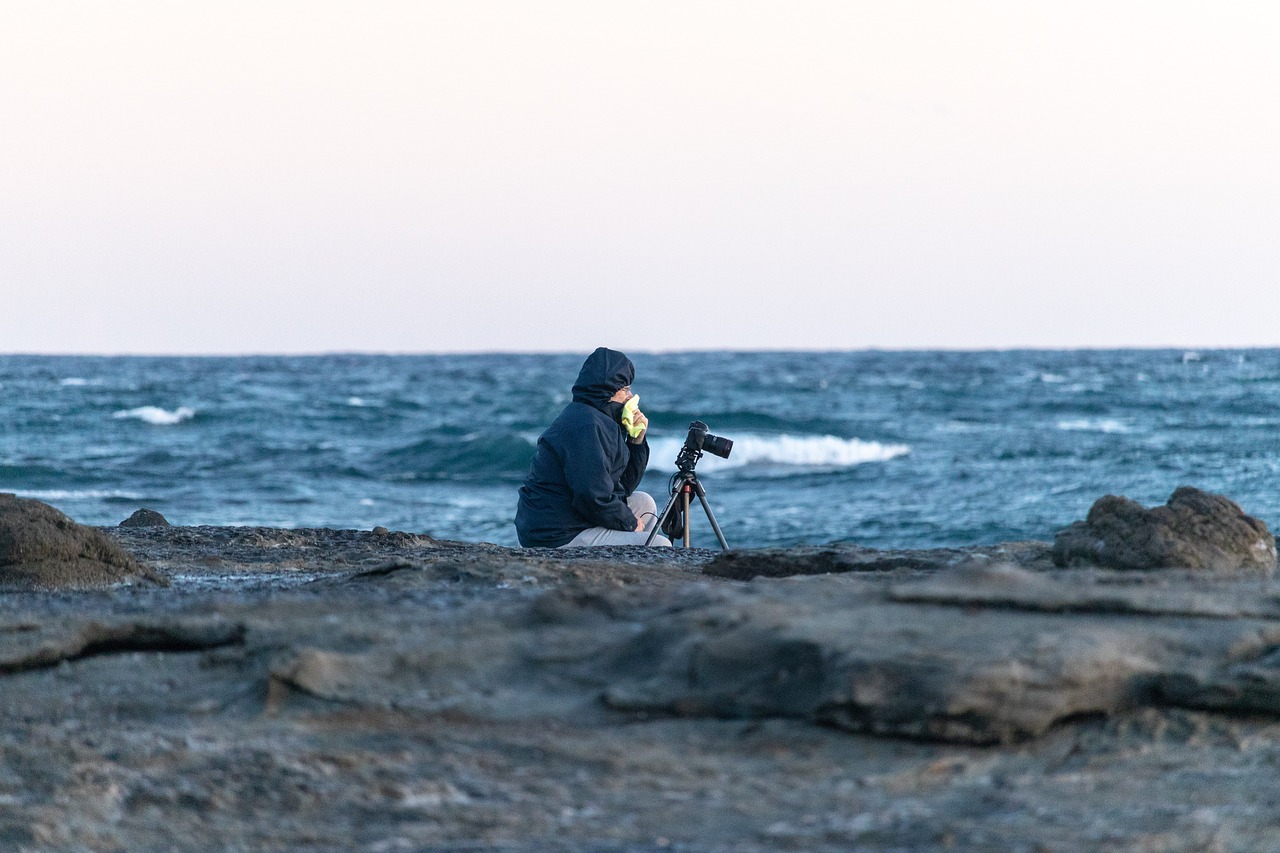 a man sitting on top of a rock next to the ocean, a picture, by Peter Churcher, with nikon cameras, 2 0 0 mm telephoto, fully covered, taking a picture