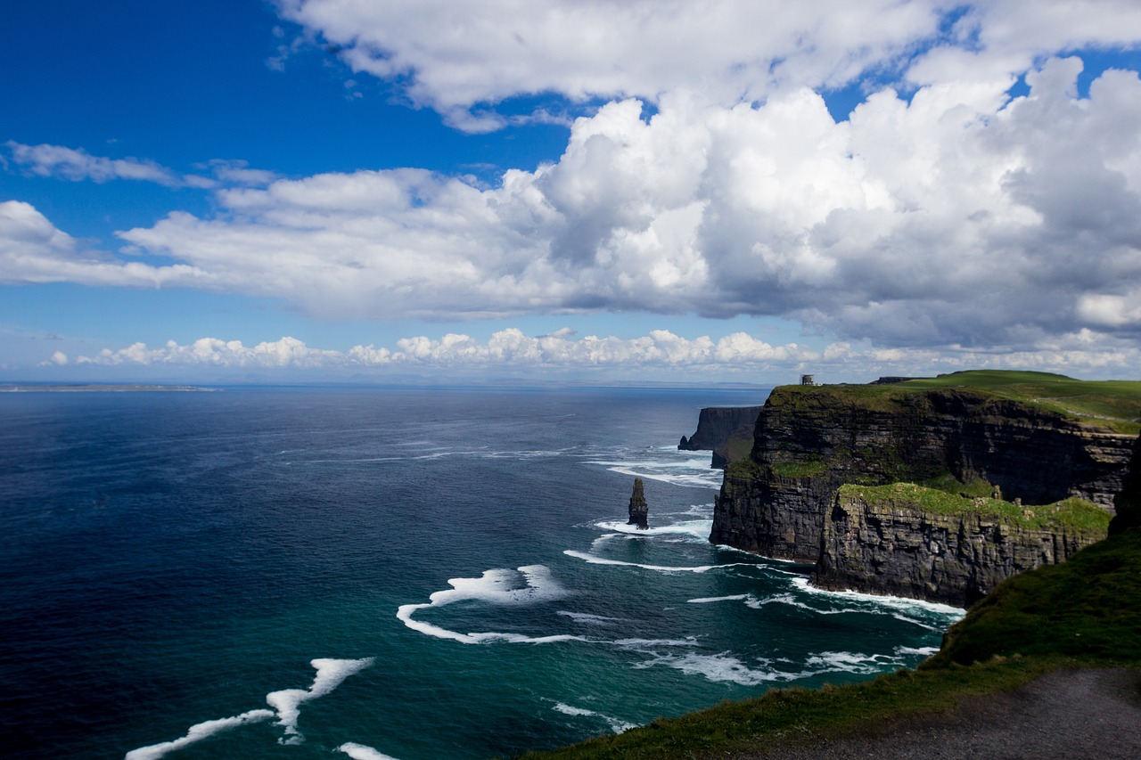 a man standing on top of a cliff next to the ocean, a tilt shift photo, irish, harmony of swirly clouds, three towers, photo of a beautiful