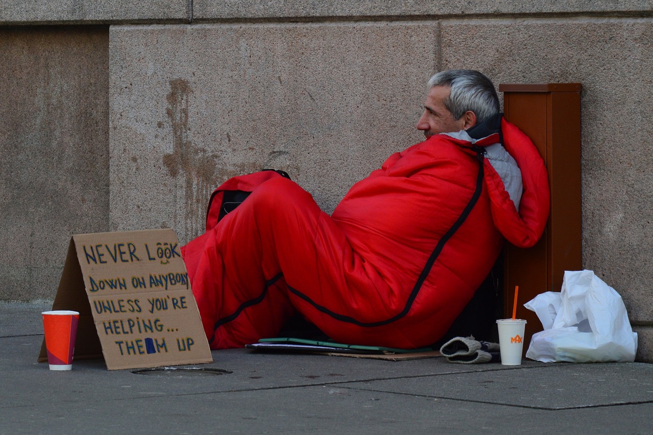 a man in a sleeping bag sitting on the sidewalk, a photo, red and black suit, in london, 3 4 5 3 1, a friend in need