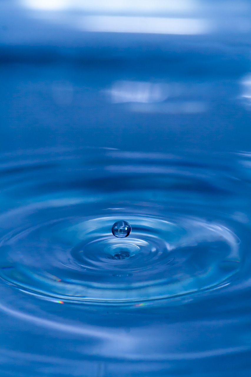 a close up of a water drop in a body of water, minimalism, rippling electromagnetic, blue background colour, spherical, sapphire