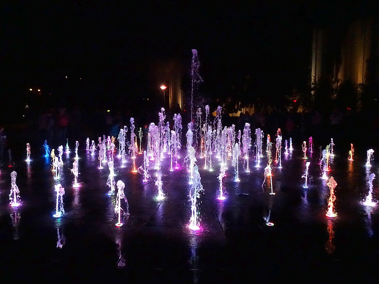 a group of people standing around a fountain of water, a hologram, night colors, crowded square, on a sunny day, photo taken at night