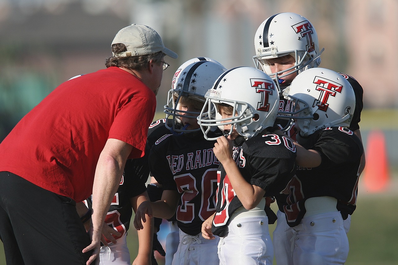 a group of young football players standing on top of a field, by Paul Davis, shutterstock, half helmet, red white and black color scheme, dad, licking