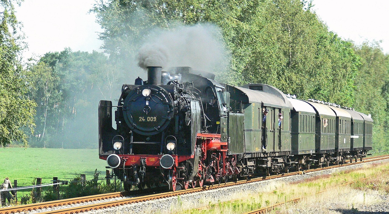 a train traveling down train tracks next to a lush green field, a portrait, by Werner Gutzeit, pixabay, romanticism, brass and steam technology, blazing engines, lower saxony, hot summer sun