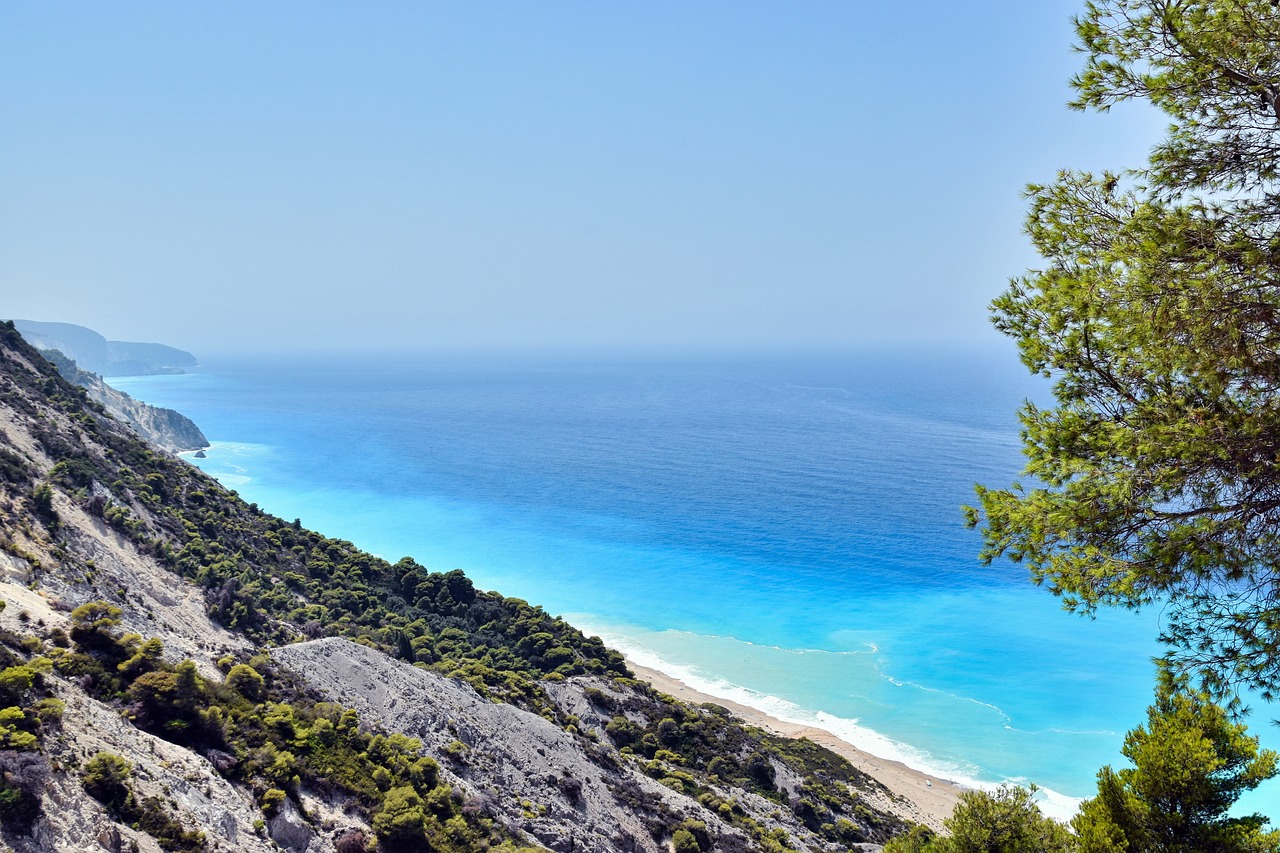 a view of the ocean from the top of a mountain, a picture, by Julian Allen, shutterstock, mediterranean beach background, silver and blue colors, onyx, beach trees in the background