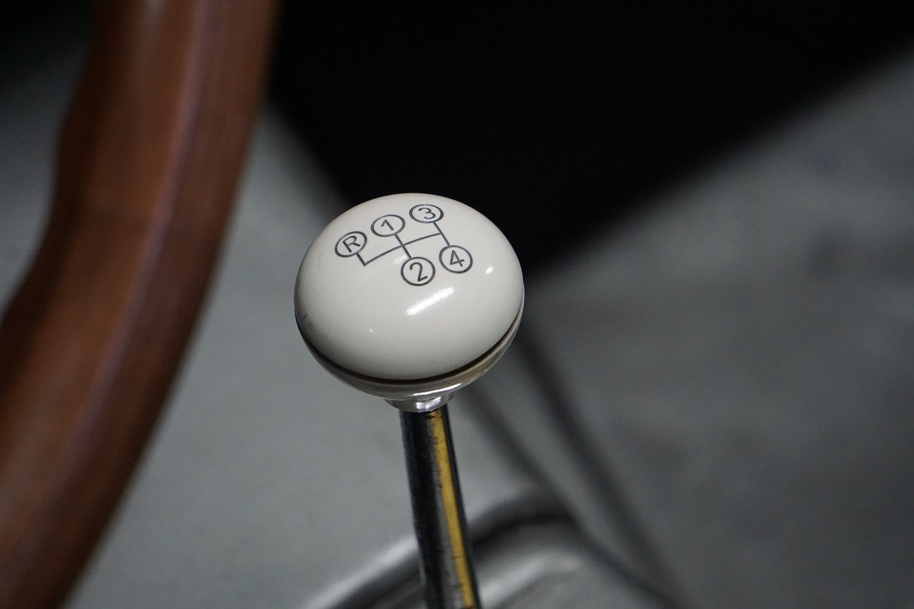 a close up of a gear stick in a car, by David Simpson, purism, pale milky white porcelain skin, kanji insignia and numbering, made of swiss cheese wheels, featuring rhodium wires