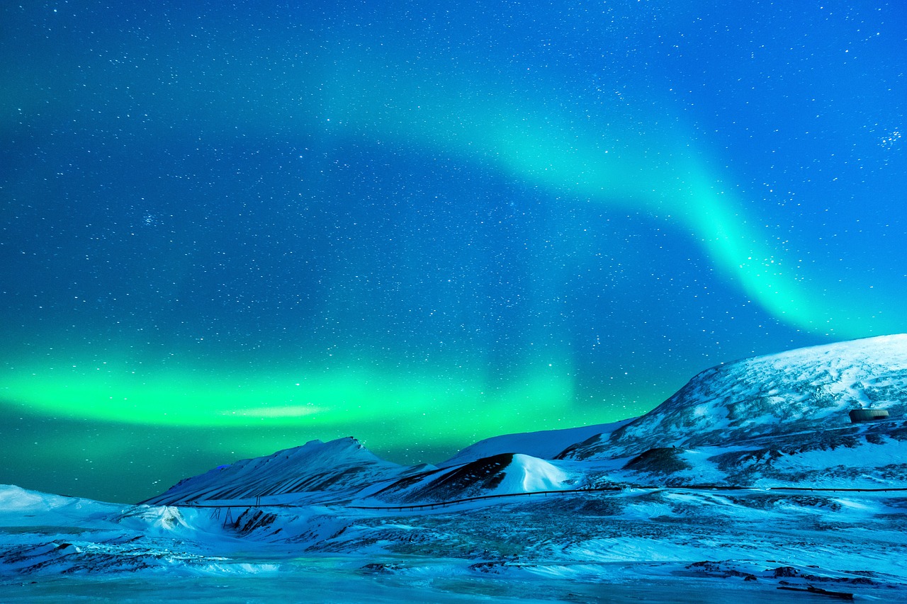 a group of people standing on top of a snow covered mountain, a matte painting, inspired by Johan Christian Dahl, shutterstock, northern lights background, distant mountains lights photo, stock photo, blue and green colours