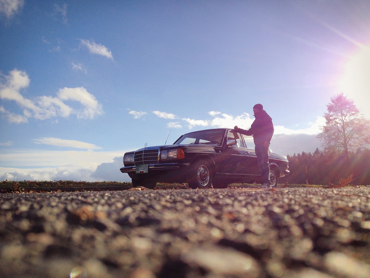 a man standing next to a parked car, a picture, by Jaakko Mattila, unsplash, photorealism, sunflare, mercedes, movie footage, wide angle 1981