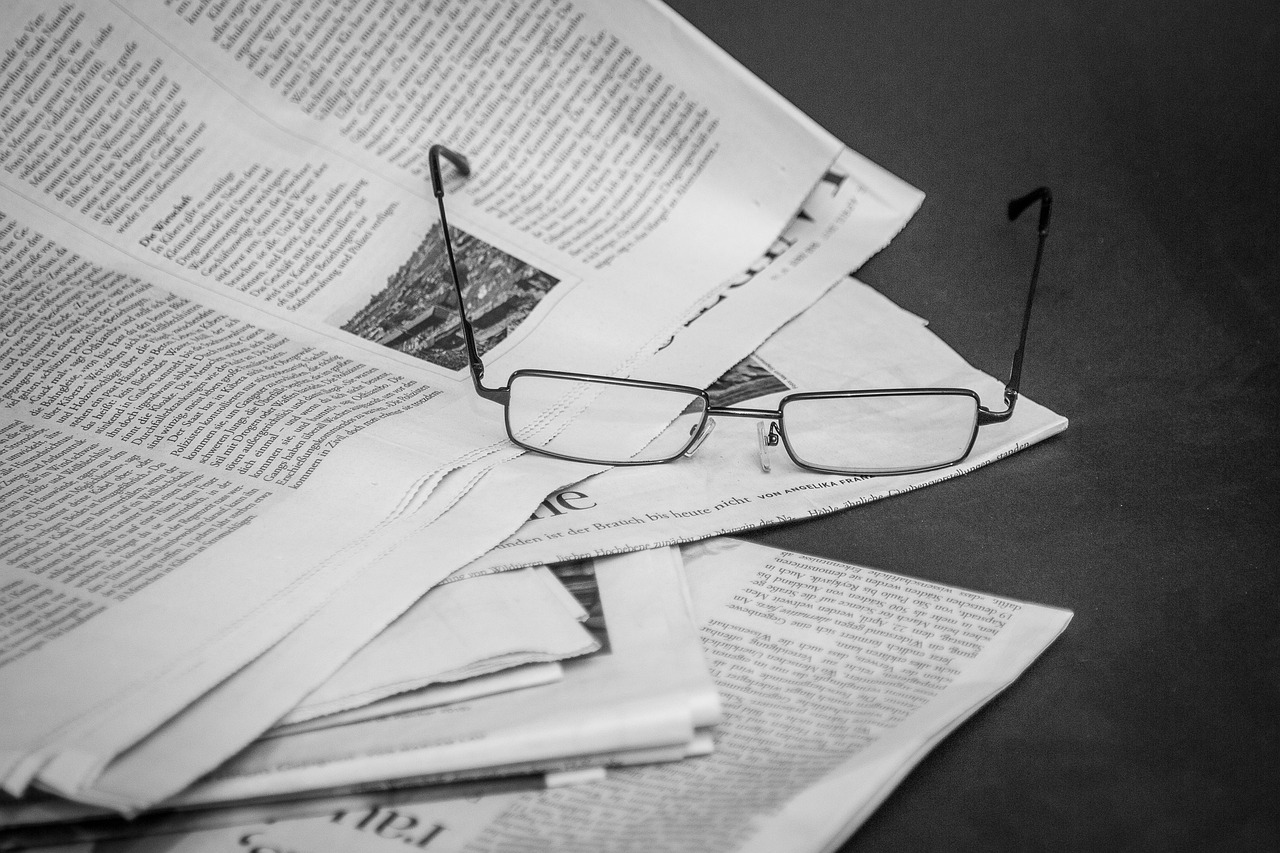 a pair of glasses sitting on top of a pile of newspapers, a black and white photo, by Maksimilijan Vanka, pexels, private press, taken with sony alpha 9, tabloid photo, portrait photo, an ancient