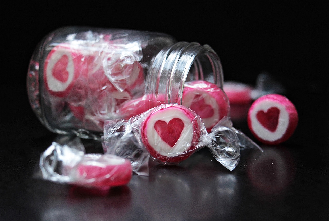 a jar filled with candy sitting on top of a table, a picture, by Sylvia Wishart, pexels, photorealism, hearts symbol, jello, with a black background, covered with pink marzipan