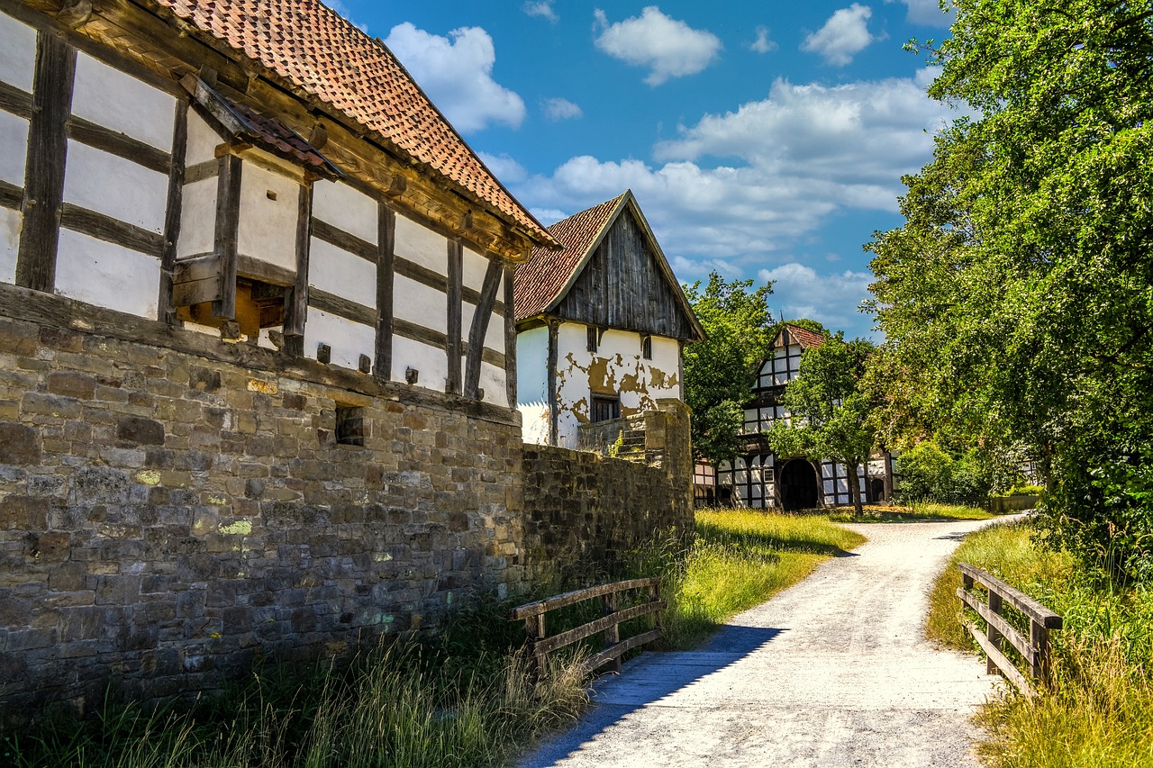 a dirt road in front of a stone building, a picture, by Karl Hagedorn, shutterstock, timbered house with bricks, hot summer day, abandoned barn in the background, castle wall