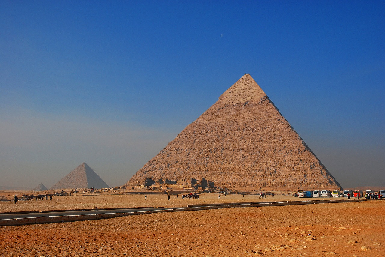 a group of people standing in front of a pyramid, egyptian art, by Kurt Roesch, pexels, two giant towers, clear blue skies, viewed from a distance, shai-hulud