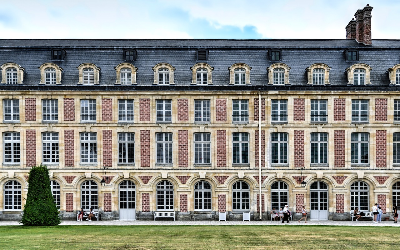 a group of people sitting on a bench in front of a building, by Raphaël Collin, shutterstock, paris school, located in a castle, wide long view, brick building, 1128x191 resolution