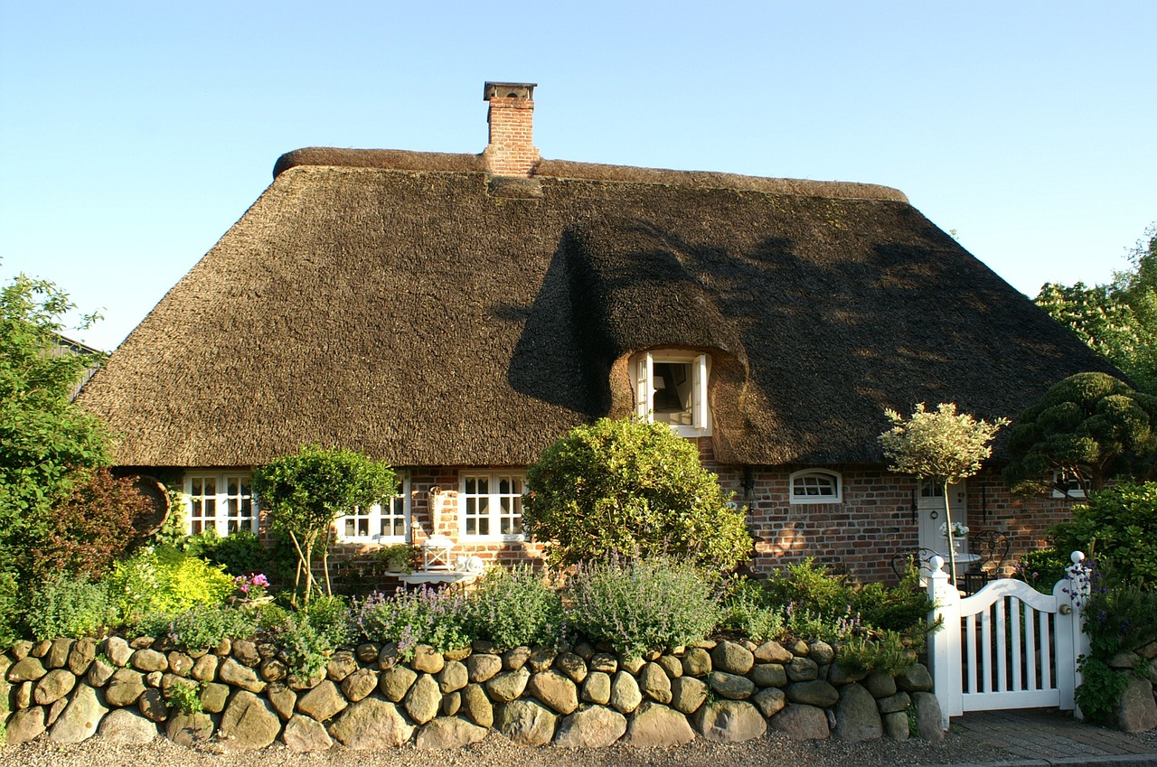 a house with a thatched roof next to a stone wall, by Karl Hagedorn, pixabay, low dutch angle, hedges, tar - like, cape