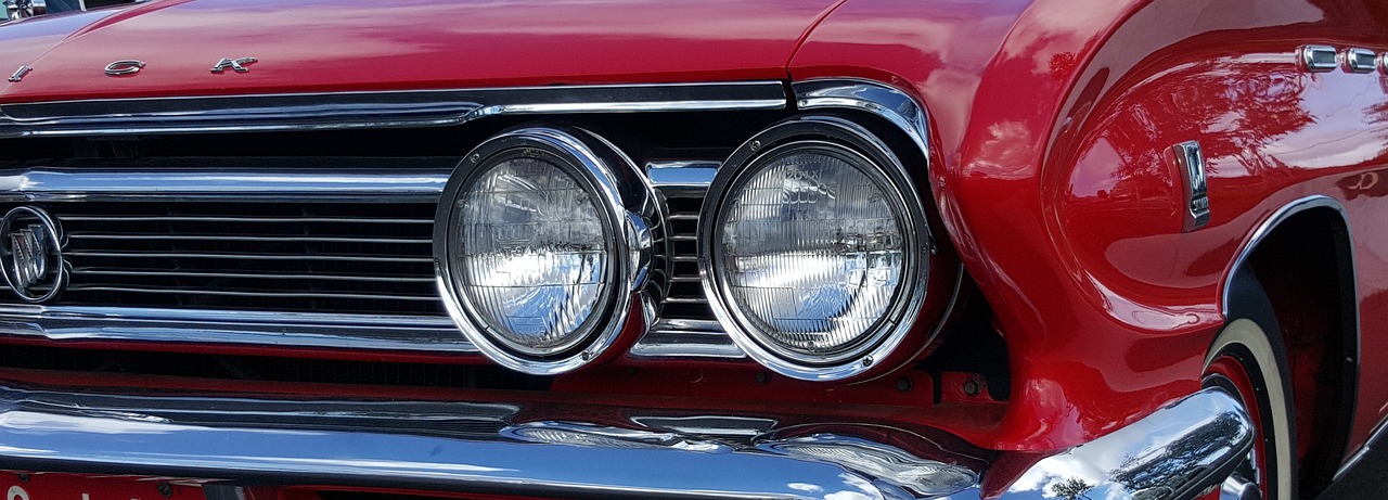 a close up of the front end of a red car, a portrait, by Tom Carapic, pixabay, round headlights, 1 9 6 5 lightning, some glints and specs, [ [ hyperrealistic ] ]