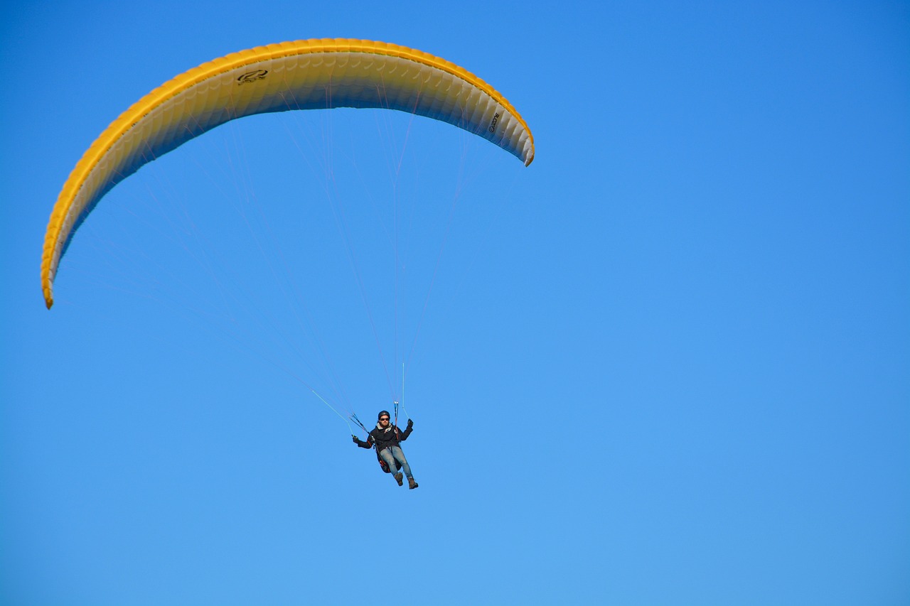 a person that is in the air with a parachute, by Niko Henrichon, flickr, yellow and blue color scheme, maui, hunting, clear blue skies