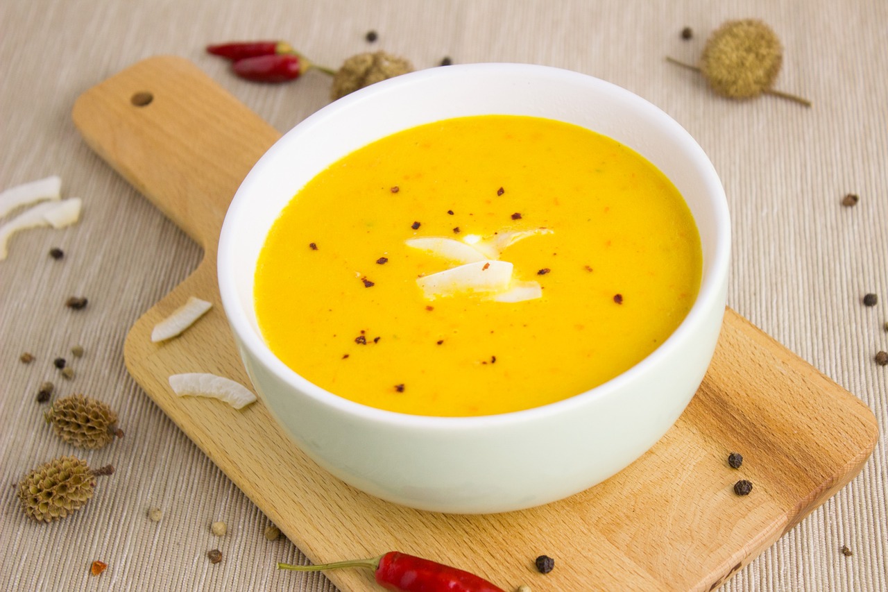 a bowl of soup sitting on top of a wooden cutting board, inspired by Géza Dósa, yellow and ornage color scheme, food particles, high quality product image”, pepper