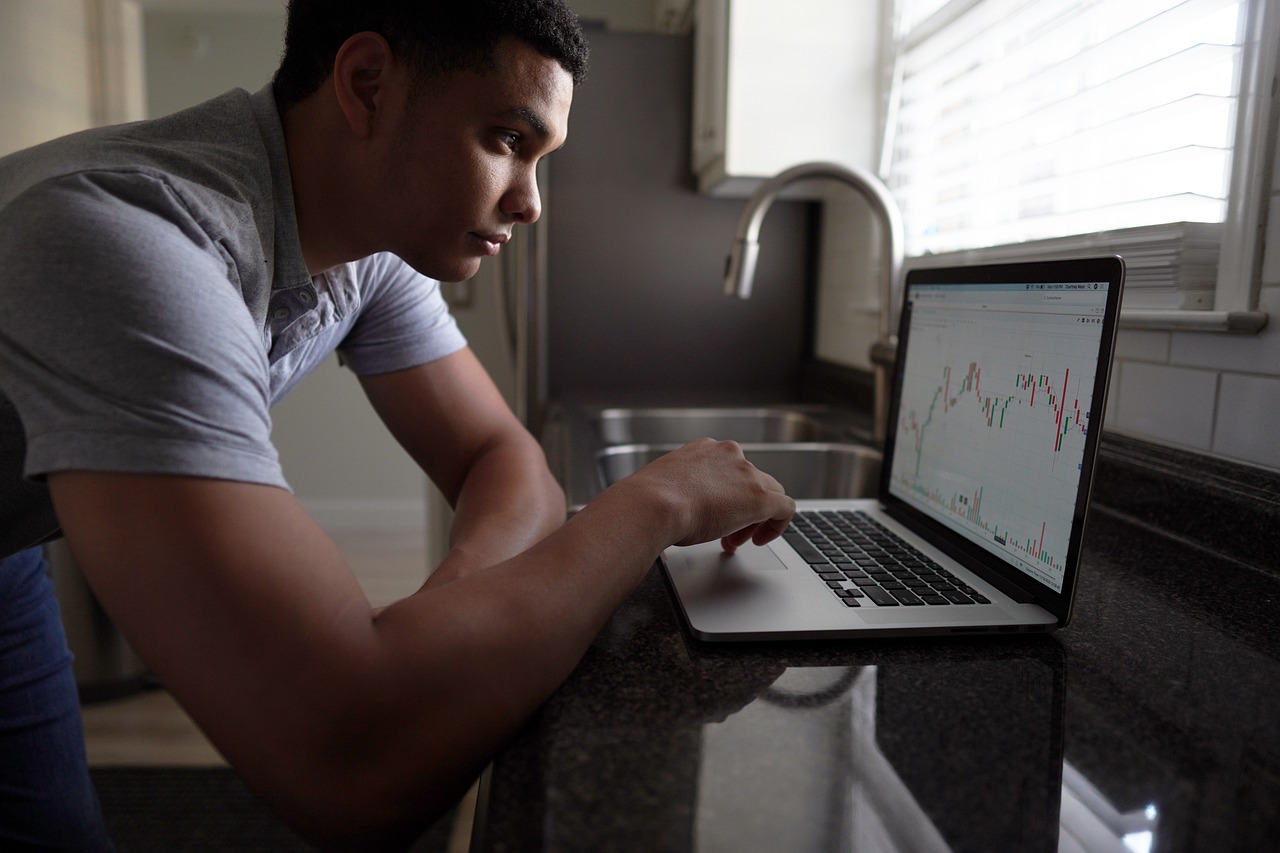 a man using a laptop computer in a kitchen, by Byron Galvez, displaying stock charts, thoughtful pose, crypto, candid picture