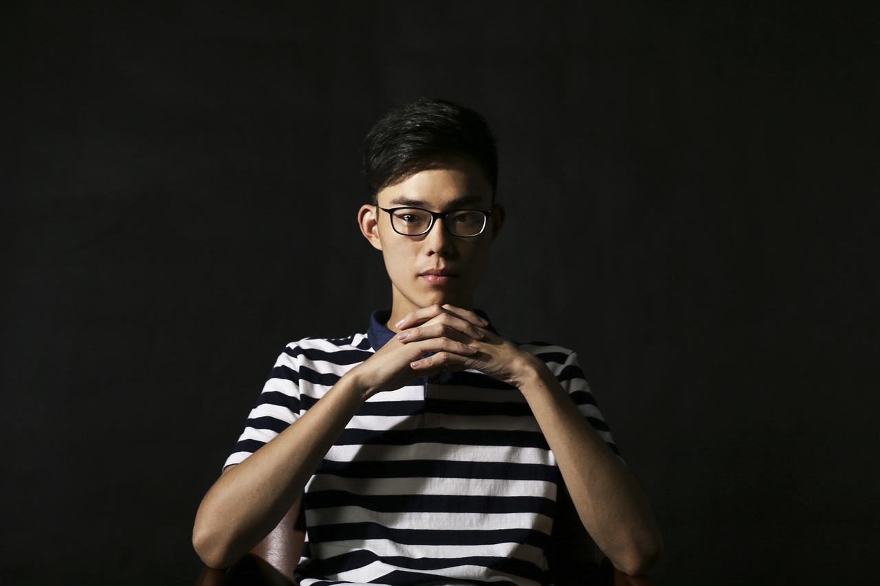 a woman wearing glasses sitting in a chair, a portrait, inspired by Ding Yunpeng, unsplash, hyperrealism, portrait of 14 years old boy, wearing stripe shirt, standing with a black background, delicate androgynous prince