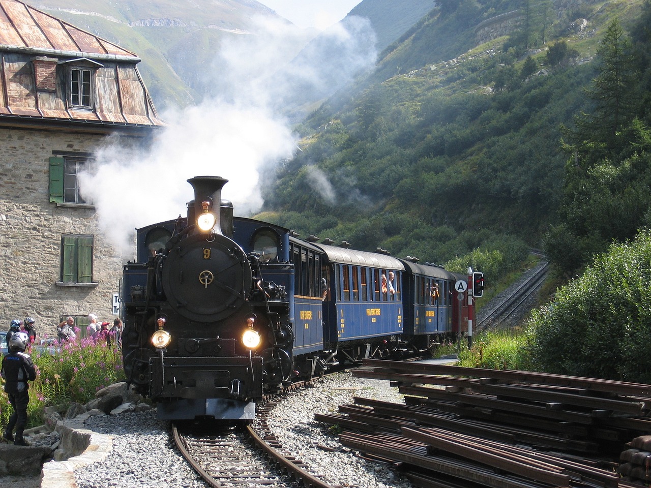 a train traveling down train tracks next to a building, by Werner Andermatt, a steam wheeler from 1880s, in the mountains, indigo, wikimedia