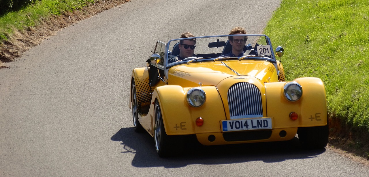 a couple of people driving a yellow car down a road, by David Simpson, flickr, prototype car, very handsome, having fun in the sun, 2014