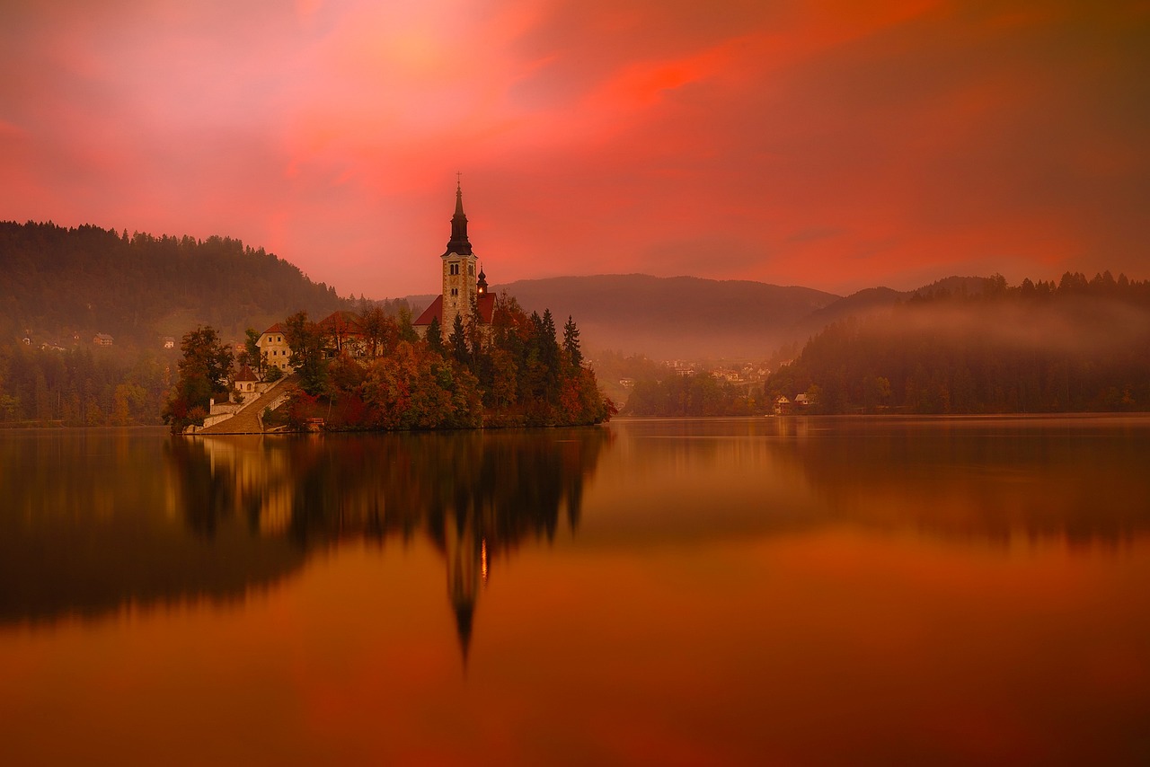 a church sitting on top of a small island in the middle of a lake, by Darek Zabrocki, romanticism, light red and orange mood, rich picturesque colors, golden mist, in shades of peach