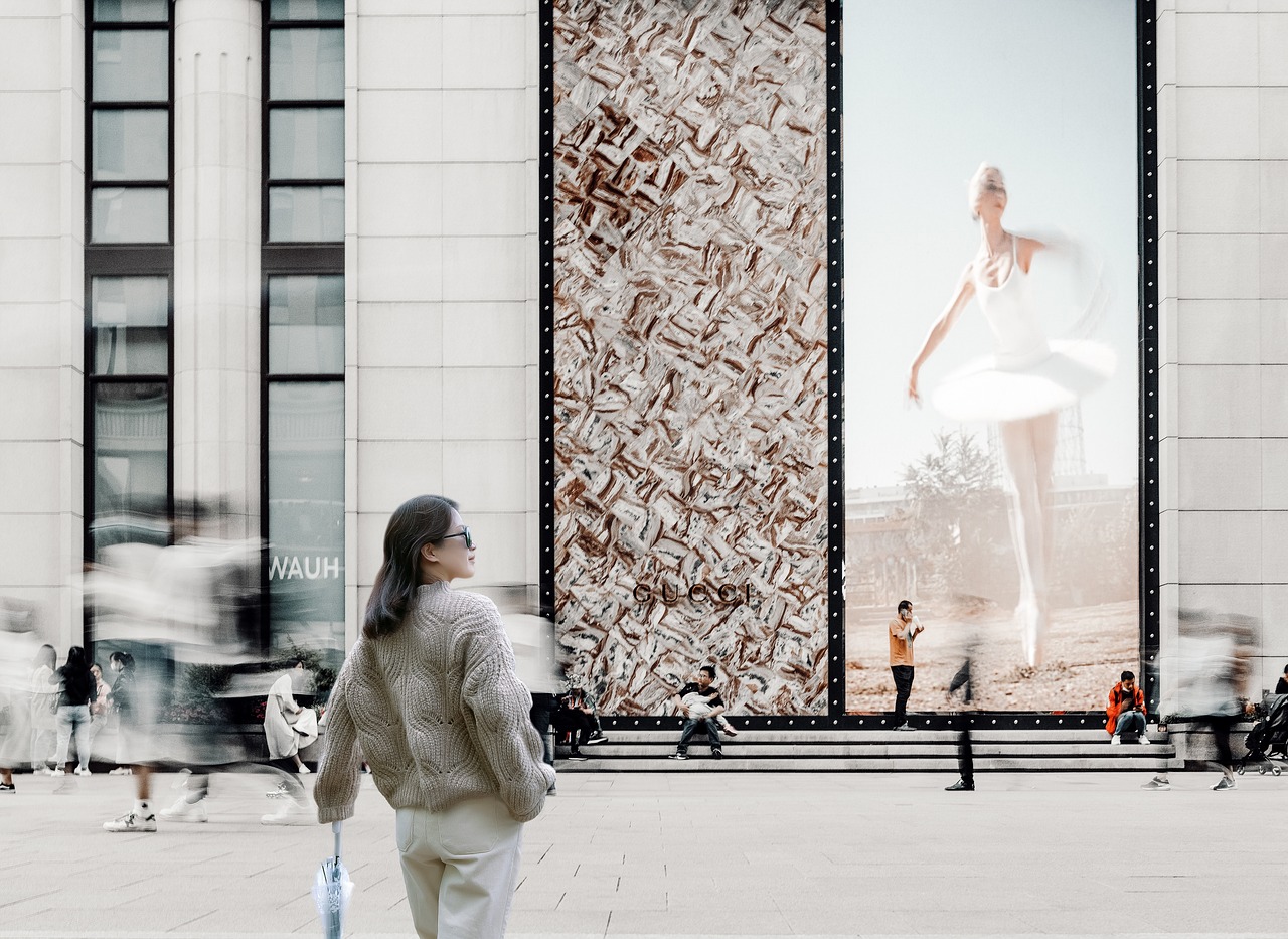 a woman walking down a sidewalk in front of a building, a picture, inspired by Anna Füssli, digital billboards, archviz, dancing in the background, interesting composition