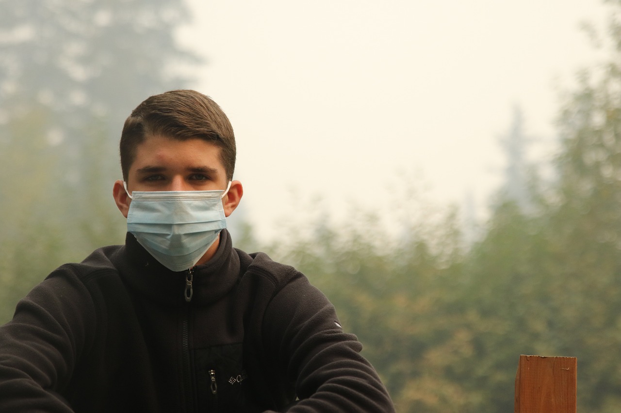 a man wearing a face mask sitting on a bench, a picture, by Attila Meszlenyi, shutterstock, realism, forest fire, around 1 9 years old, close up half body shot, turkey