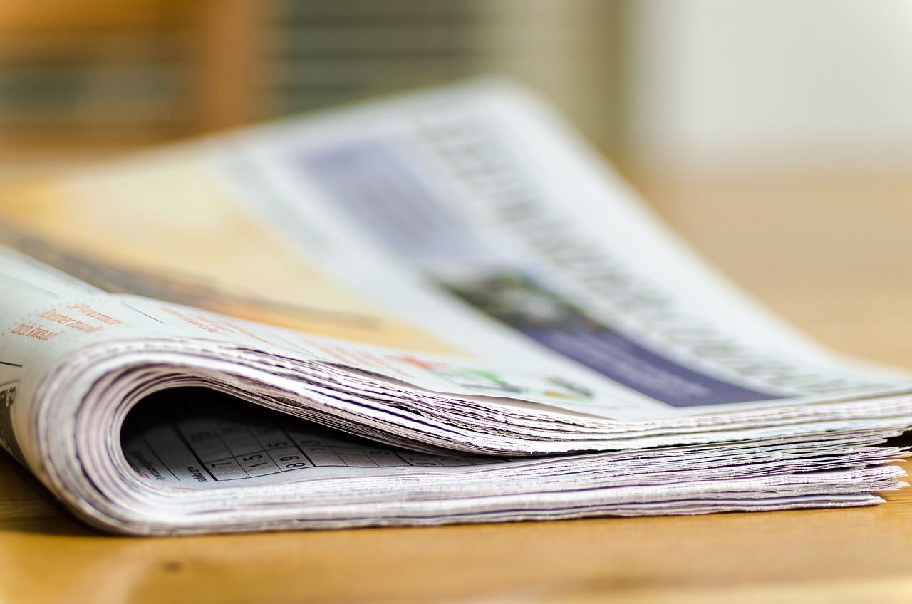 a stack of newspapers sitting on top of a wooden table, a picture, by Julian Allen, shutterstock, close macro photo. studio photo, advertisment, blurred detail, ad image