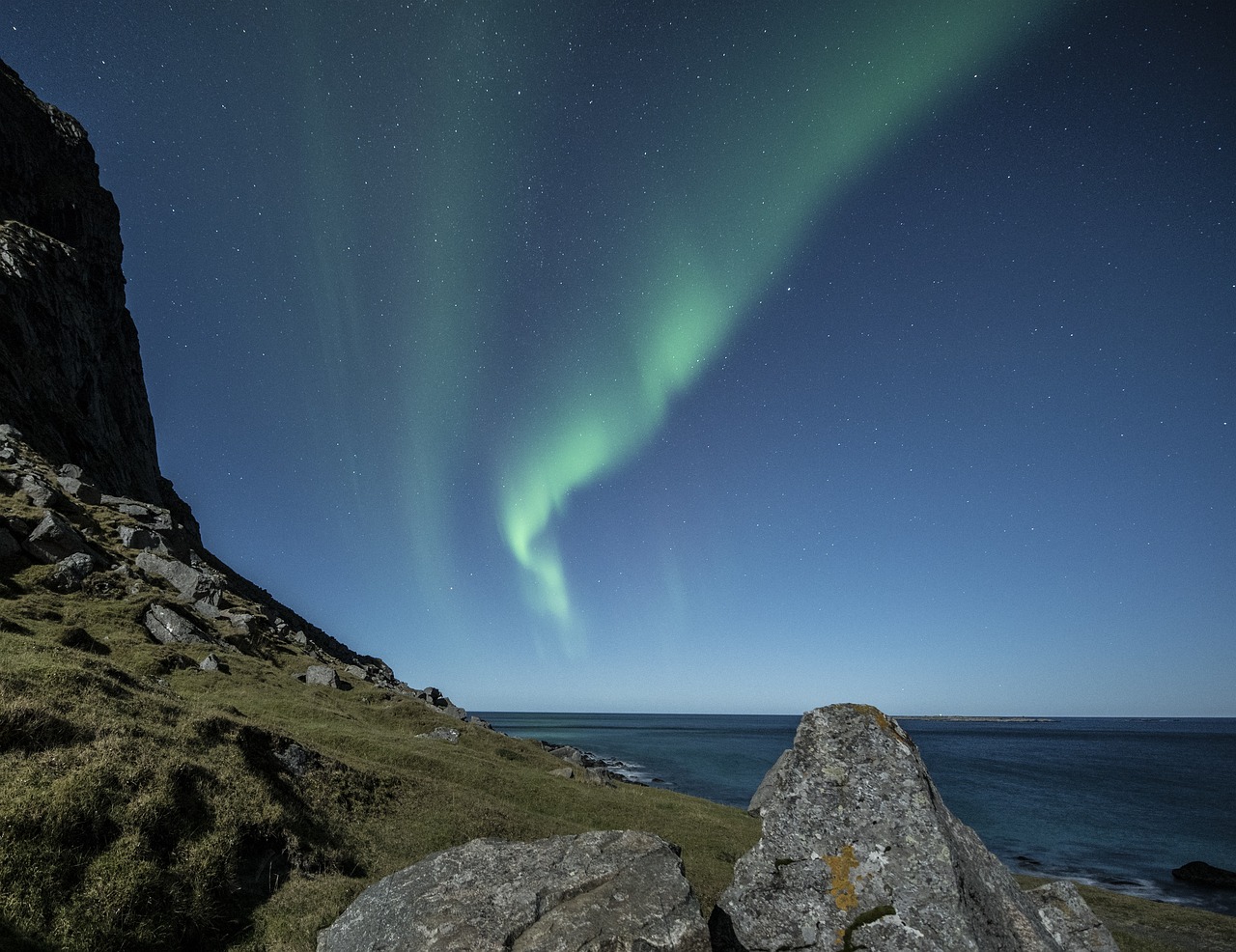 a large rock sitting on top of a lush green hillside, by Erwin Bowien, pexels, northern lights background, the night sky is a sea, arcs, november