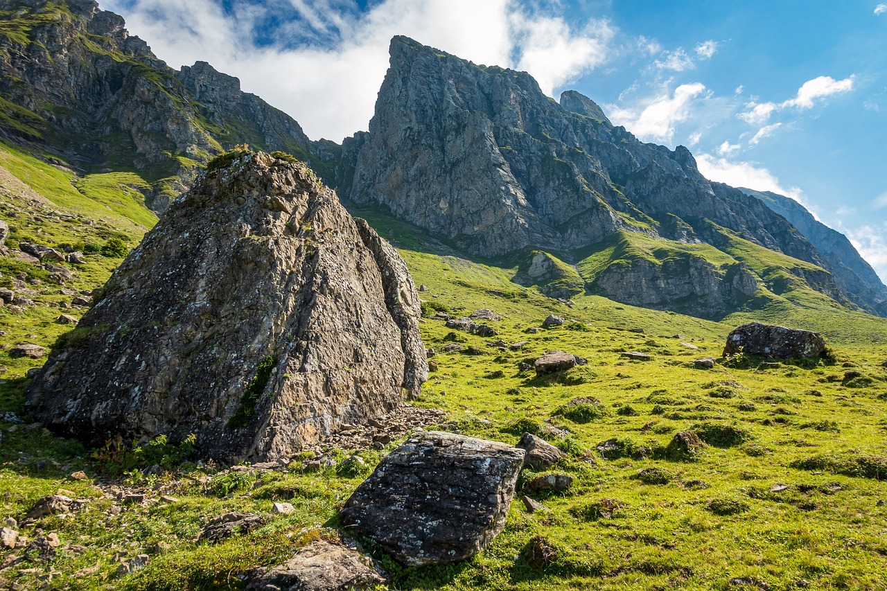 a group of rocks sitting on top of a lush green hillside, a picture, by Emanuel Büchel, shutterstock, mountain behind meadow, crib goch!!!!!!!!!!! ridge, giant imposing mountain, bottom view