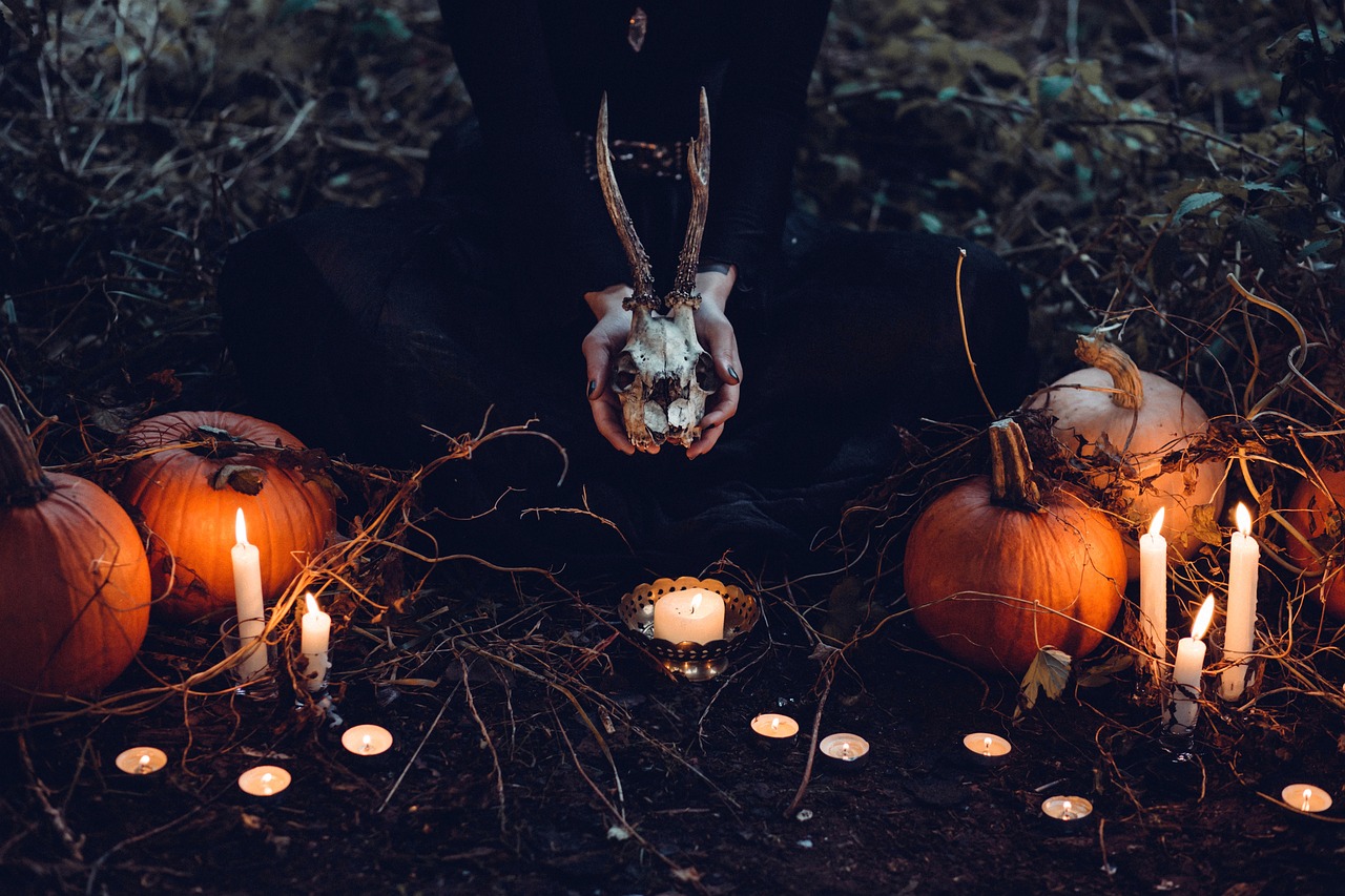 a person holding a deer skull surrounded by pumpkins and candles, unsplash contest winner, vanitas, wearing gothic accessories, orange and black tones, with cobwebs, inside covens den