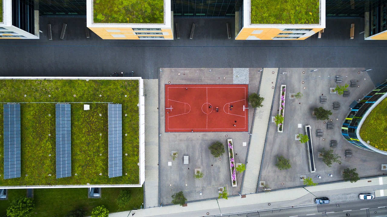 an aerial view of a basketball court surrounded by buildings, by Matthias Weischer, building cover with plant, outdoor photo