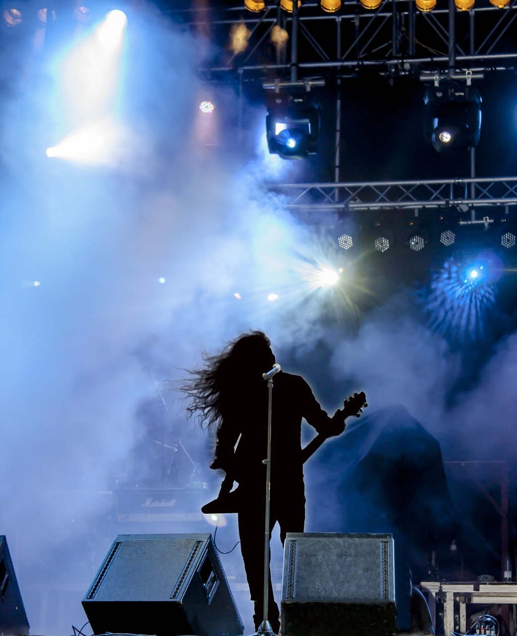 a person standing on a stage with a guitar, a picture, pexels, figuration libre, gunpowder smoke, venomize, backlit, festival