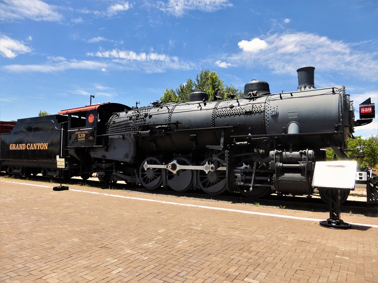 a large black train sitting on top of a train track, a portrait, at the museum, on a bright day, albuquerque, white steam on the side