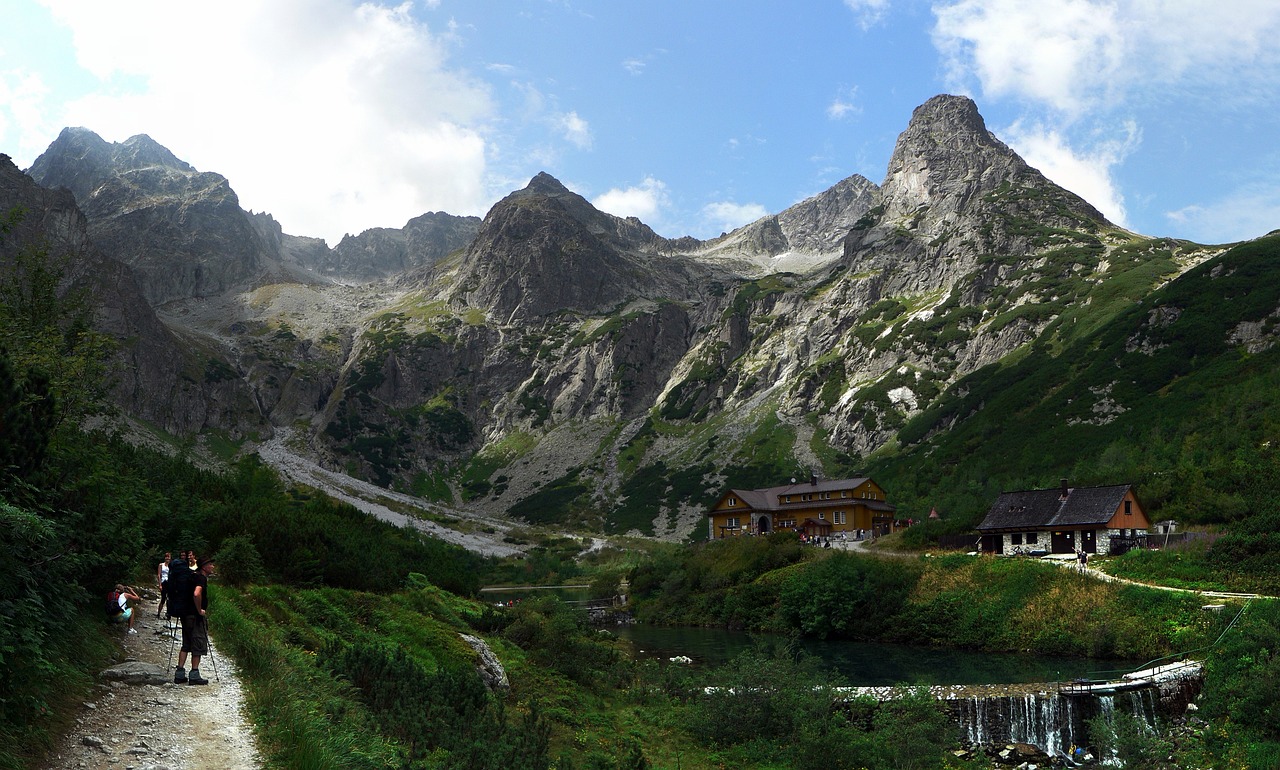 a group of people walking down a path in the mountains, by Aleksander Gierymski, flickr, small cottage in the foreground, panoramic widescreen view, ponds, bogna gawrońska