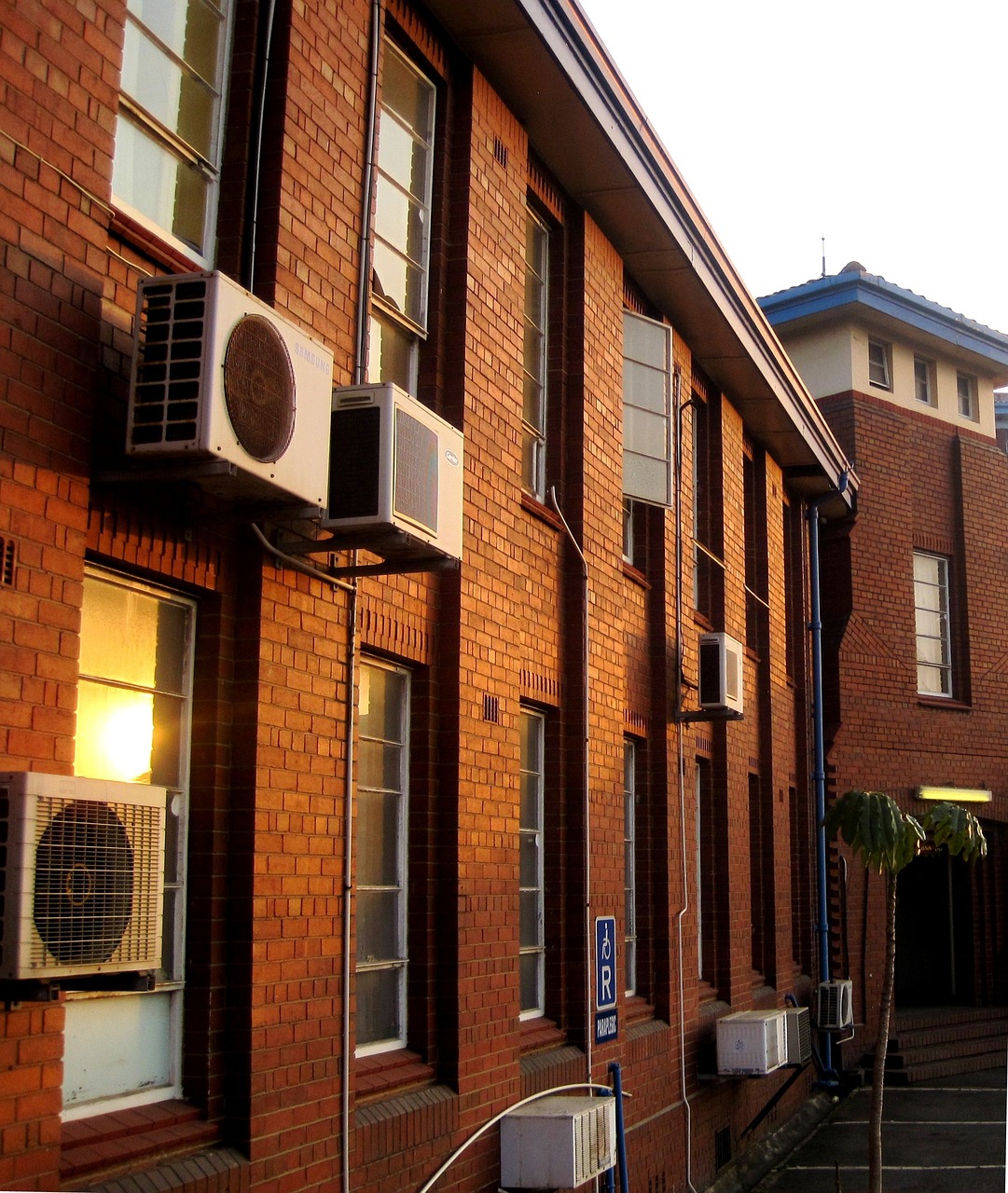 an air conditioner sitting on the side of a building, by Lee Loughridge, flickr, heidelberg school, japanese high school, brick building, warmly lit, art deco office buildings