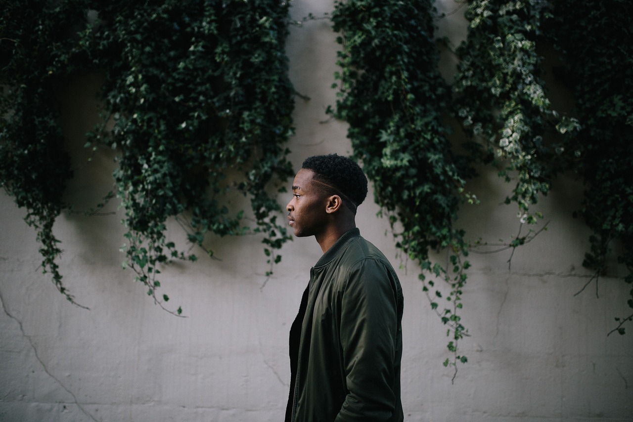 a man standing in front of a wall covered in ivys, a character portrait, inspired by Gordon Parks, unsplash, greenery, side profile centered portrait, black young woman, thin young male