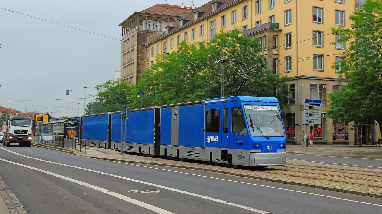 a blue train traveling down a street next to tall buildings, by Oskar Lüthy, flickr, hannover, s line, zaun, summer street