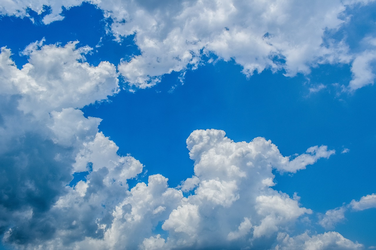 a plane flying through a cloudy blue sky, a stock photo, minimalism, prismatic cumulus clouds, low angle 8k hd nature photo, big smoke clouds visible, bright sunny day blue sky