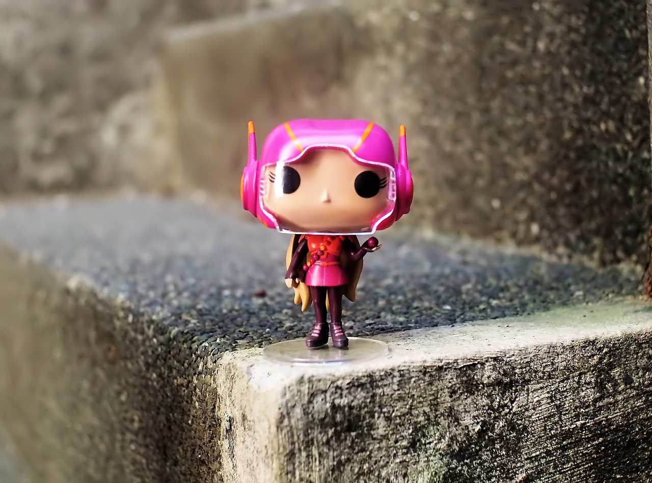a close up of a toy on a ledge, inspired by Taiyō Matsumoto, pop art, scarlet witch costume, elon musk funko pop, bright pink highlights, oversaturated lens flair